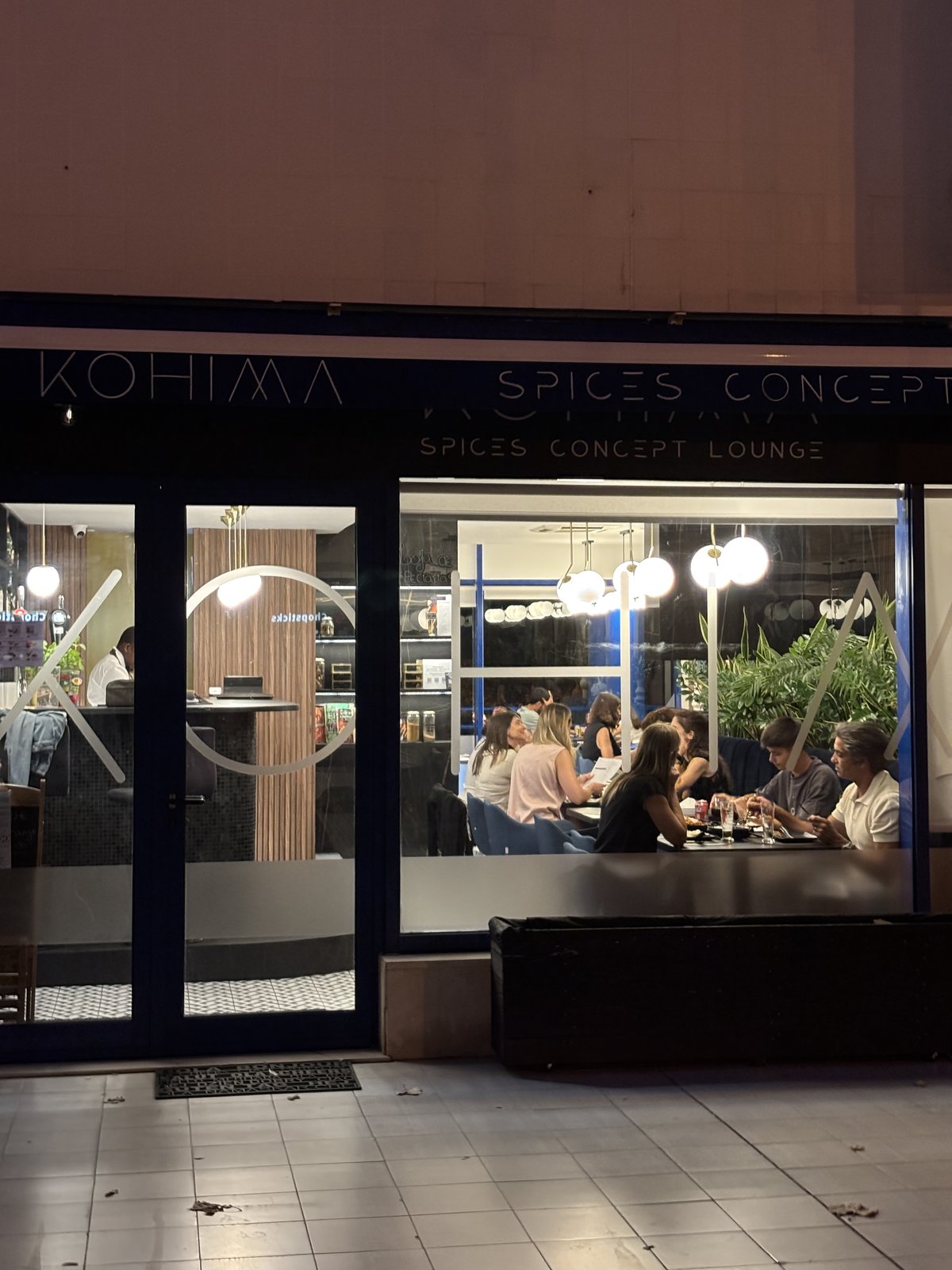 Fachada do Kohima à noite com clientes no interior